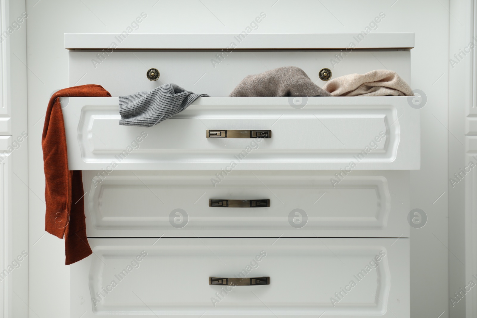 Photo of Cluttered chest of drawers indoors. Clothes in mess