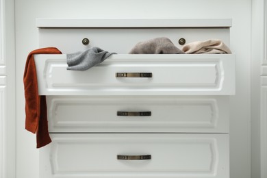 Photo of Cluttered chest of drawers indoors. Clothes in mess