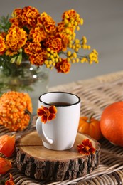 Beautiful autumn composition with cup of drink and flowers on wicker table