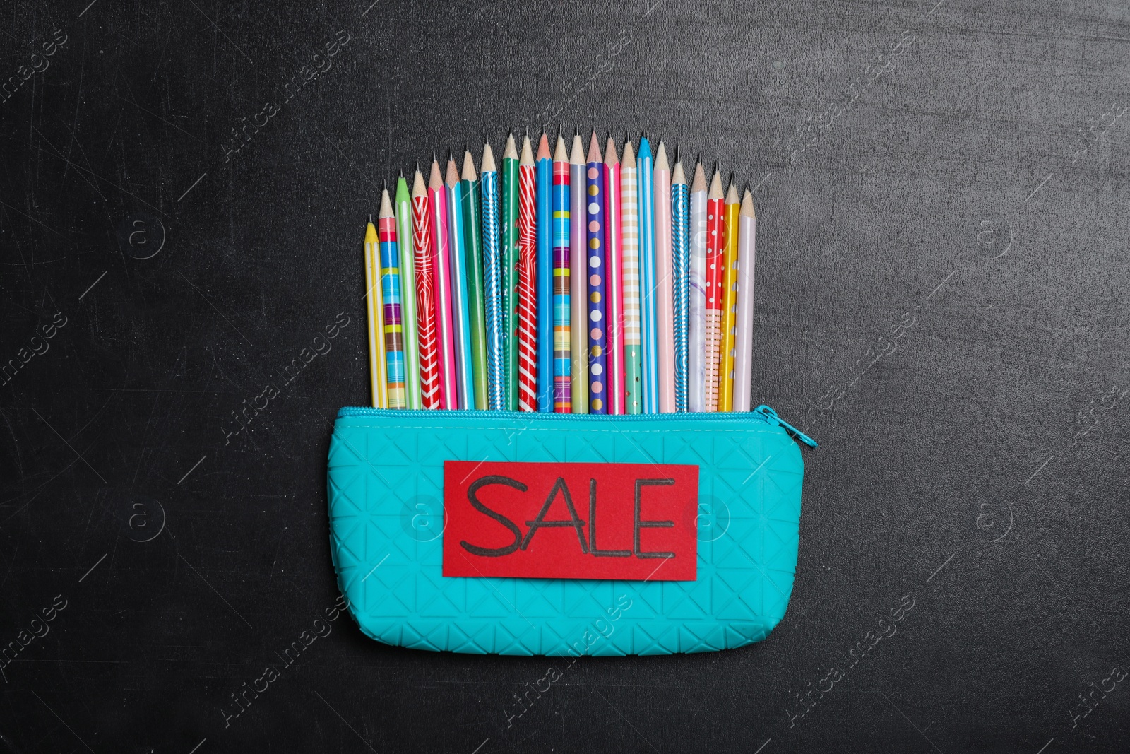 Photo of Case with different pencils and word Sale on blackboard, top view