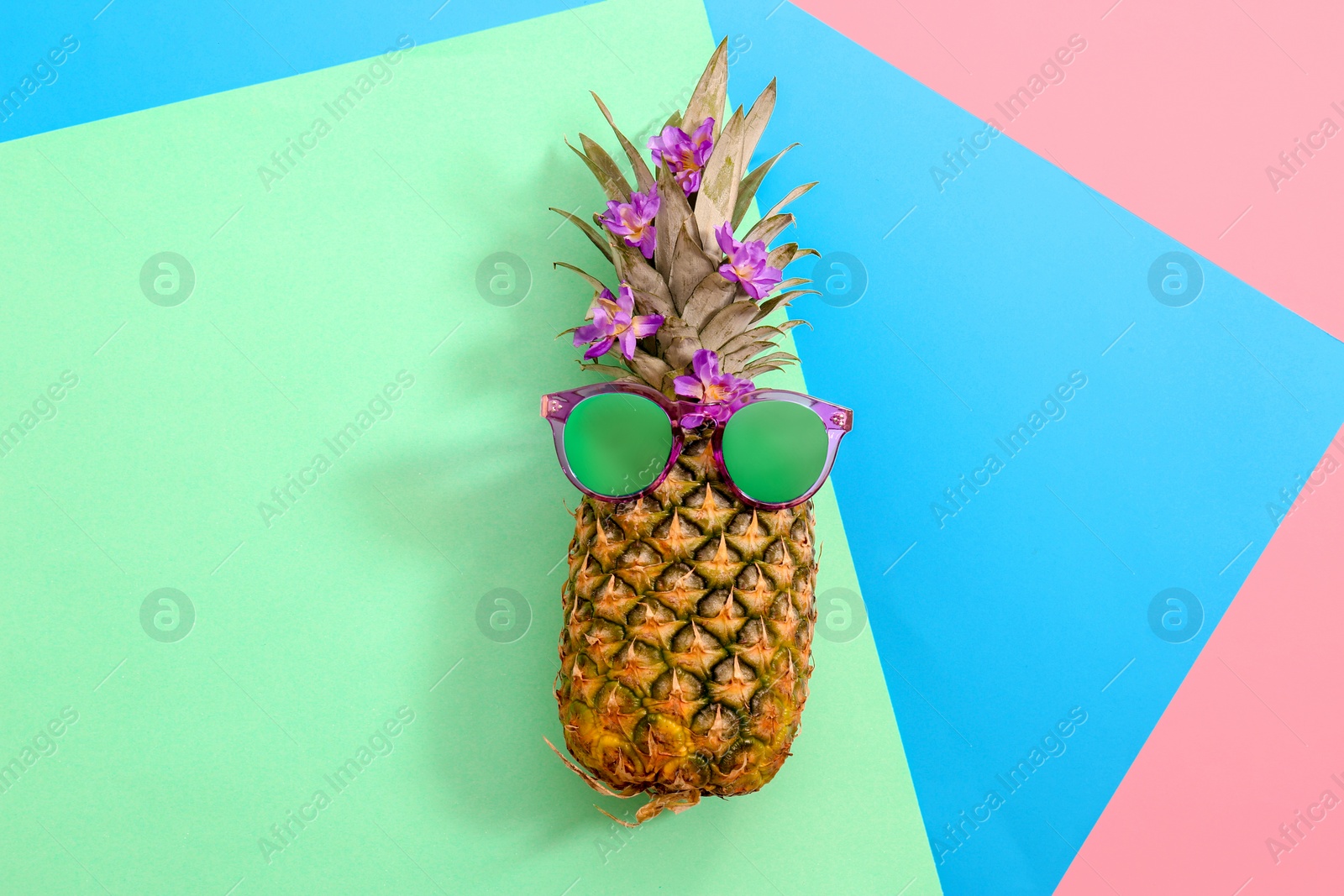 Photo of Fresh ripe pineapple with sunglasses on color background, top view