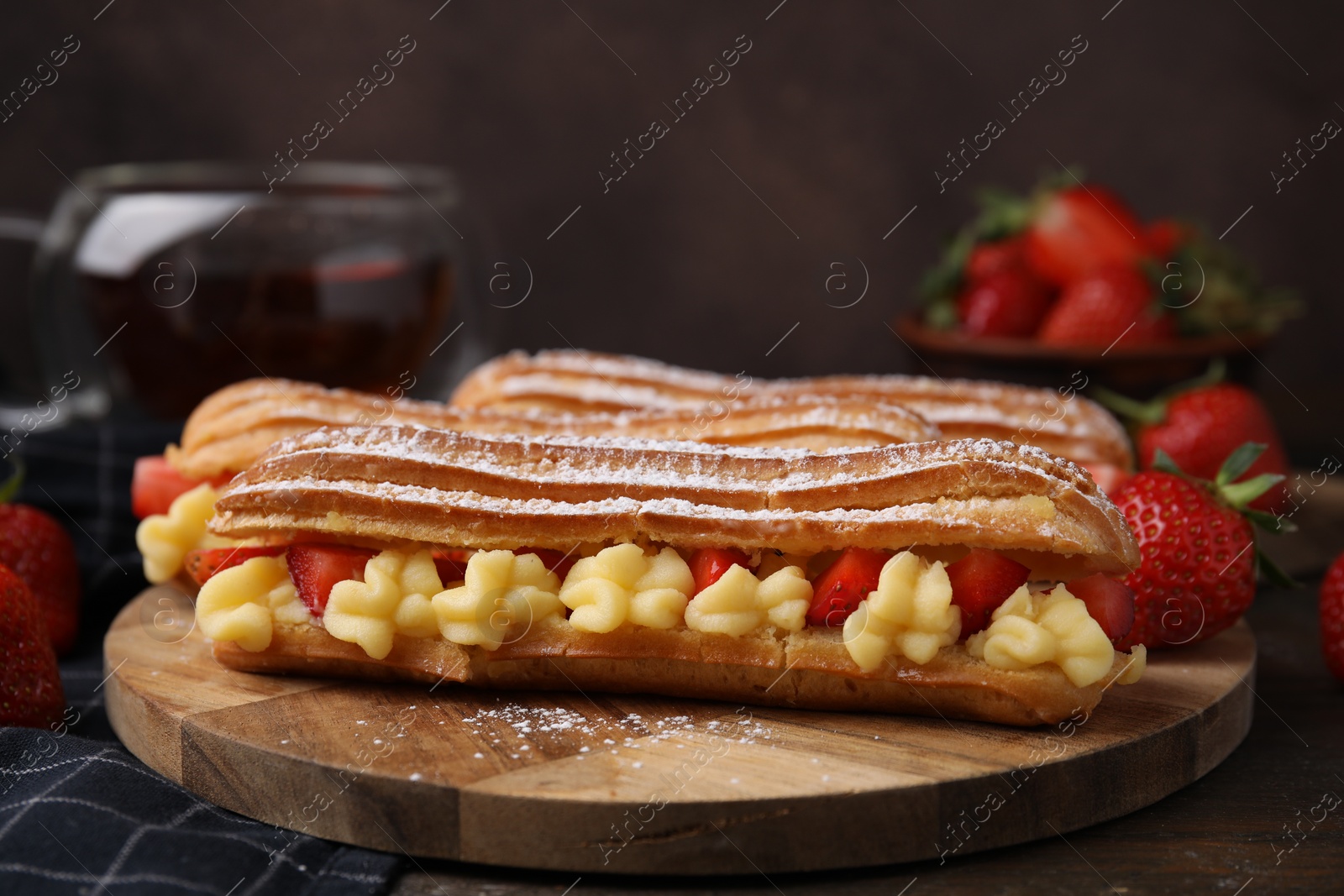 Photo of Delicious eclairs filled with cream and strawberries on wooden table