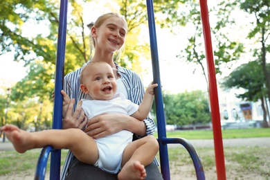 Photo of Teen nanny with cute little baby on swing outdoors