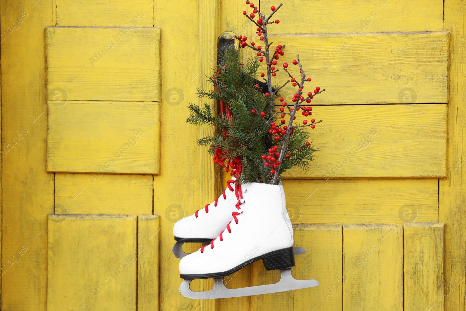 Photo of Pair of ice skates with Christmas decor hanging on old yellow door