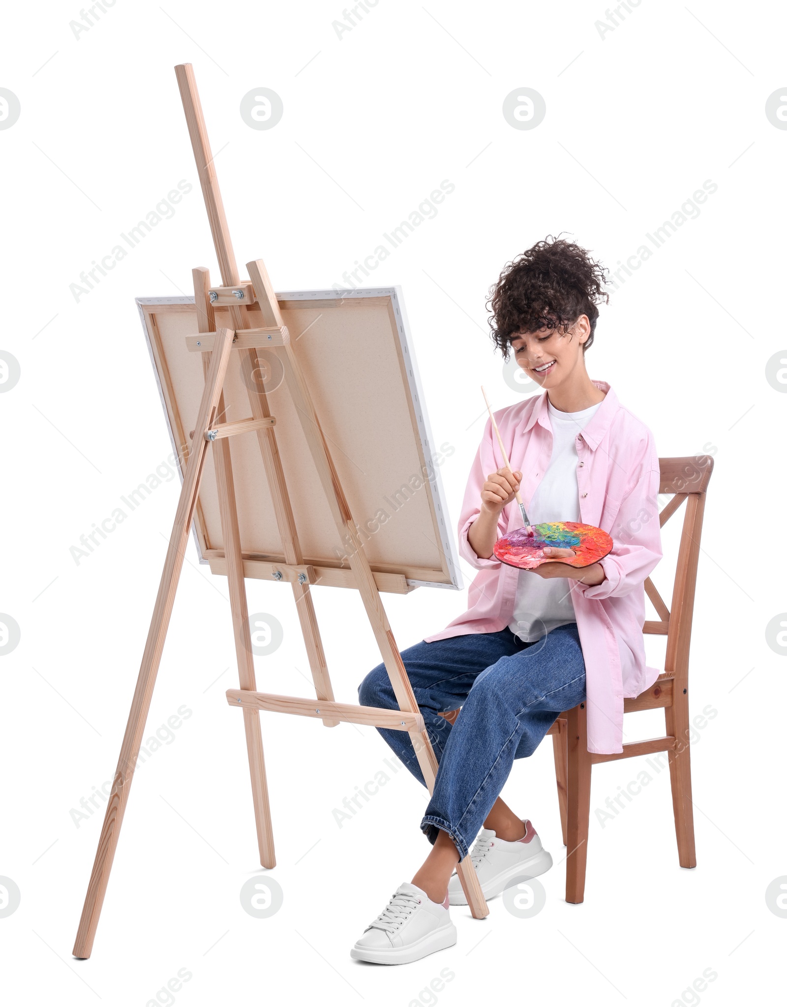 Photo of Young woman painting on easel with canvas against white background