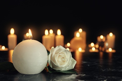 White rose and burning candle on table in darkness, space for text. Funeral symbol