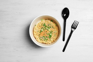 Photo of Cup of instant noodles with plastic cutlery on white wooden background, flat lay