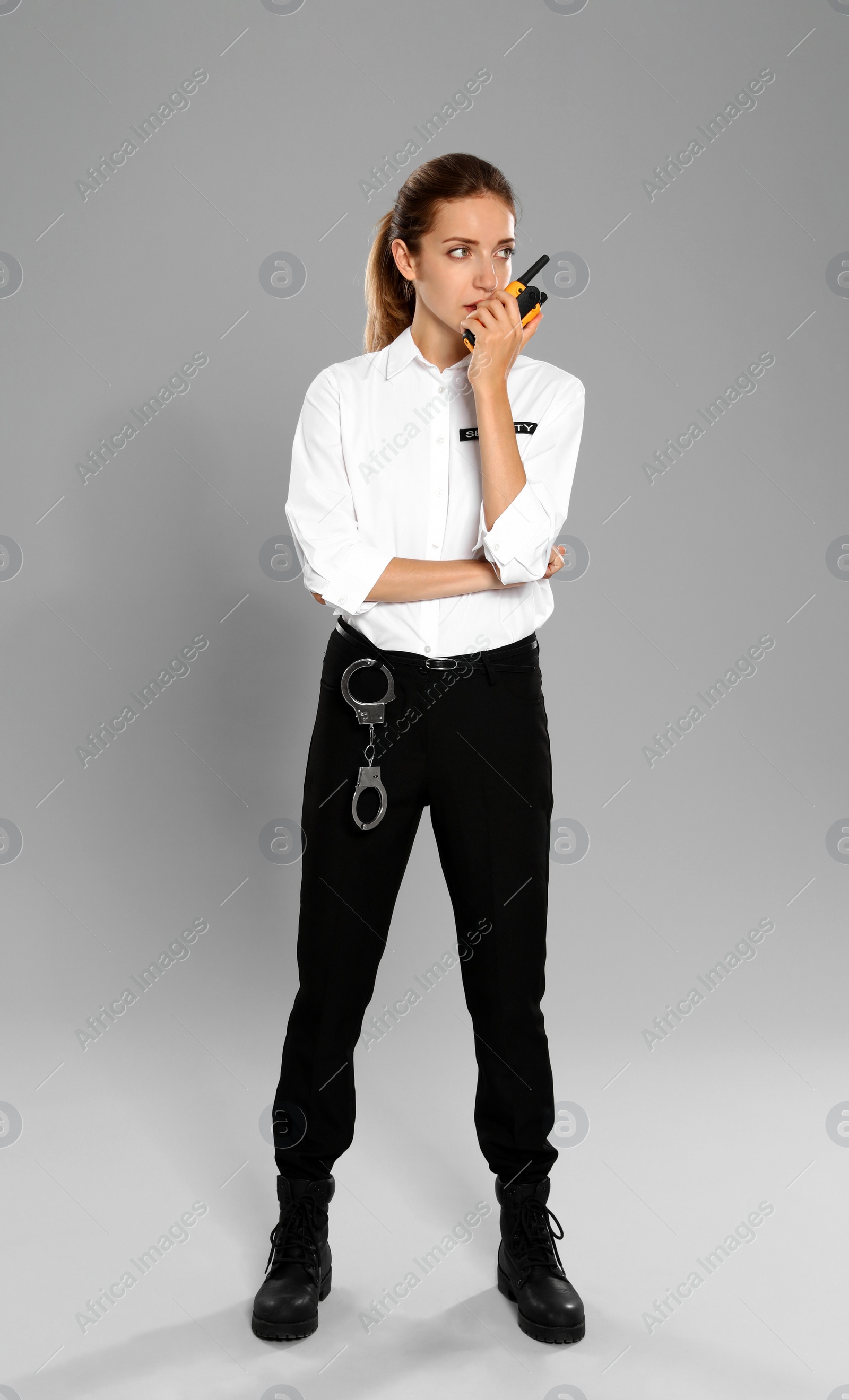 Photo of Female security guard in uniform using portable radio transmitter on grey background