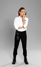 Female security guard in uniform using portable radio transmitter on grey background