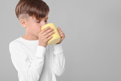 Photo of Cute boy drinking beverage from yellow ceramic mug on light grey background, space for text