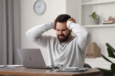 Photo of Man suffering from headache at workplace in office