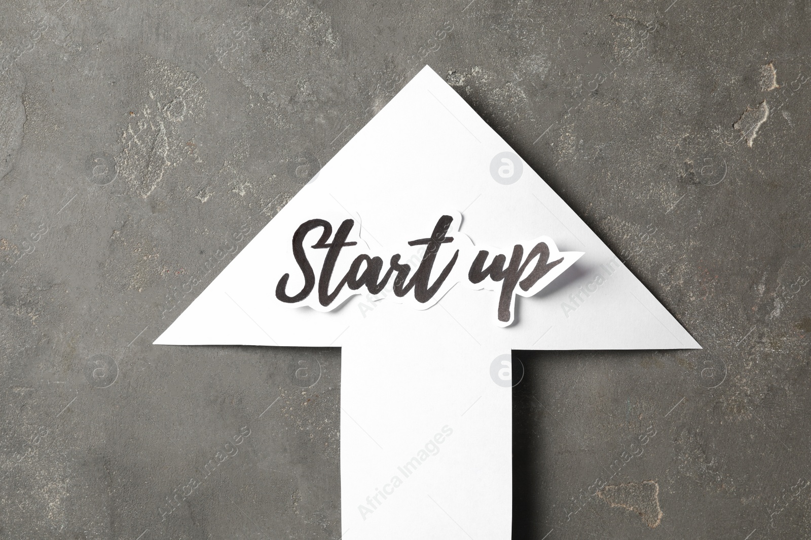 Photo of Paper arrow with phrase Start Up on grey table, top view