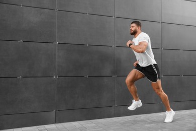 Young man running near building outdoors. Space for text