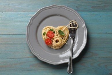 Photo of Heart made of tasty spaghetti, fork, tomato and basil on light blue wooden table, top view