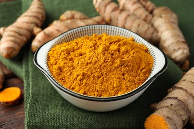 Photo of Bowl with aromatic turmeric powder and raw roots on table, closeup