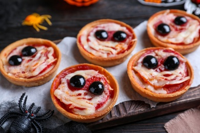 Photo of Cute monster tartlets served on black wooden table, closeup. Halloween party food