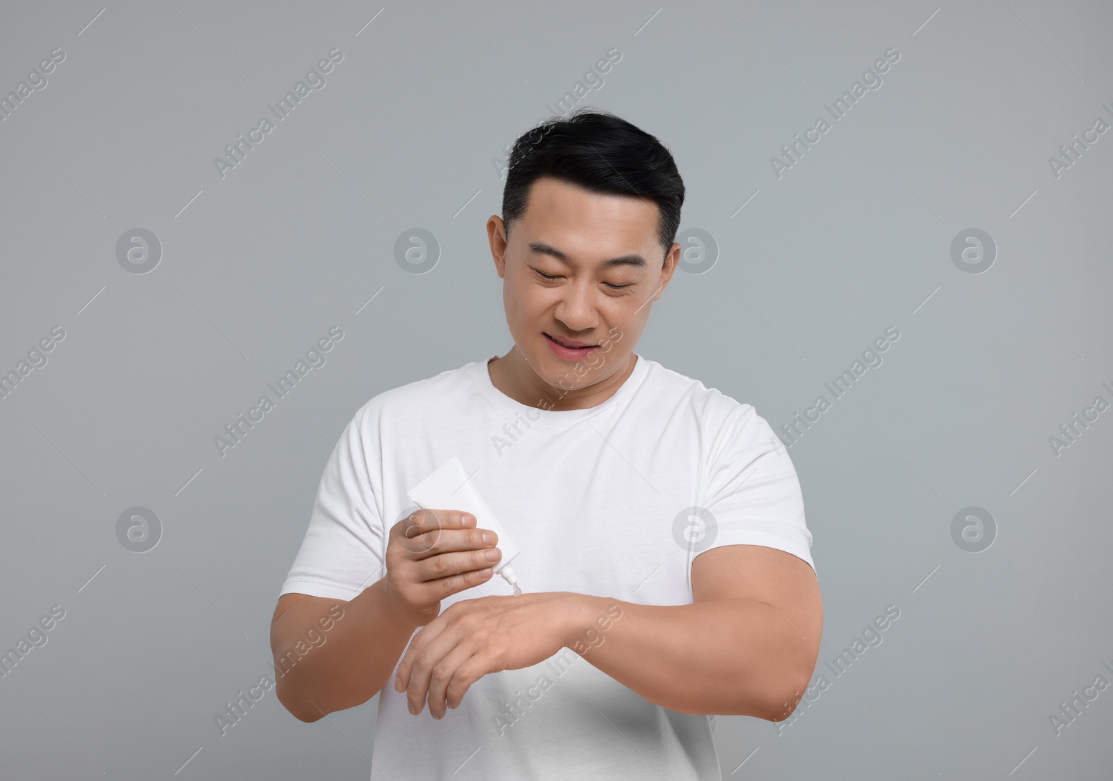 Photo of Handsome man applying body cream onto his hand on light grey background