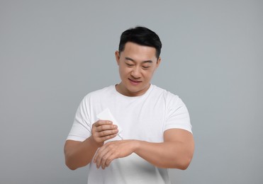 Photo of Handsome man applying body cream onto his hand on light grey background