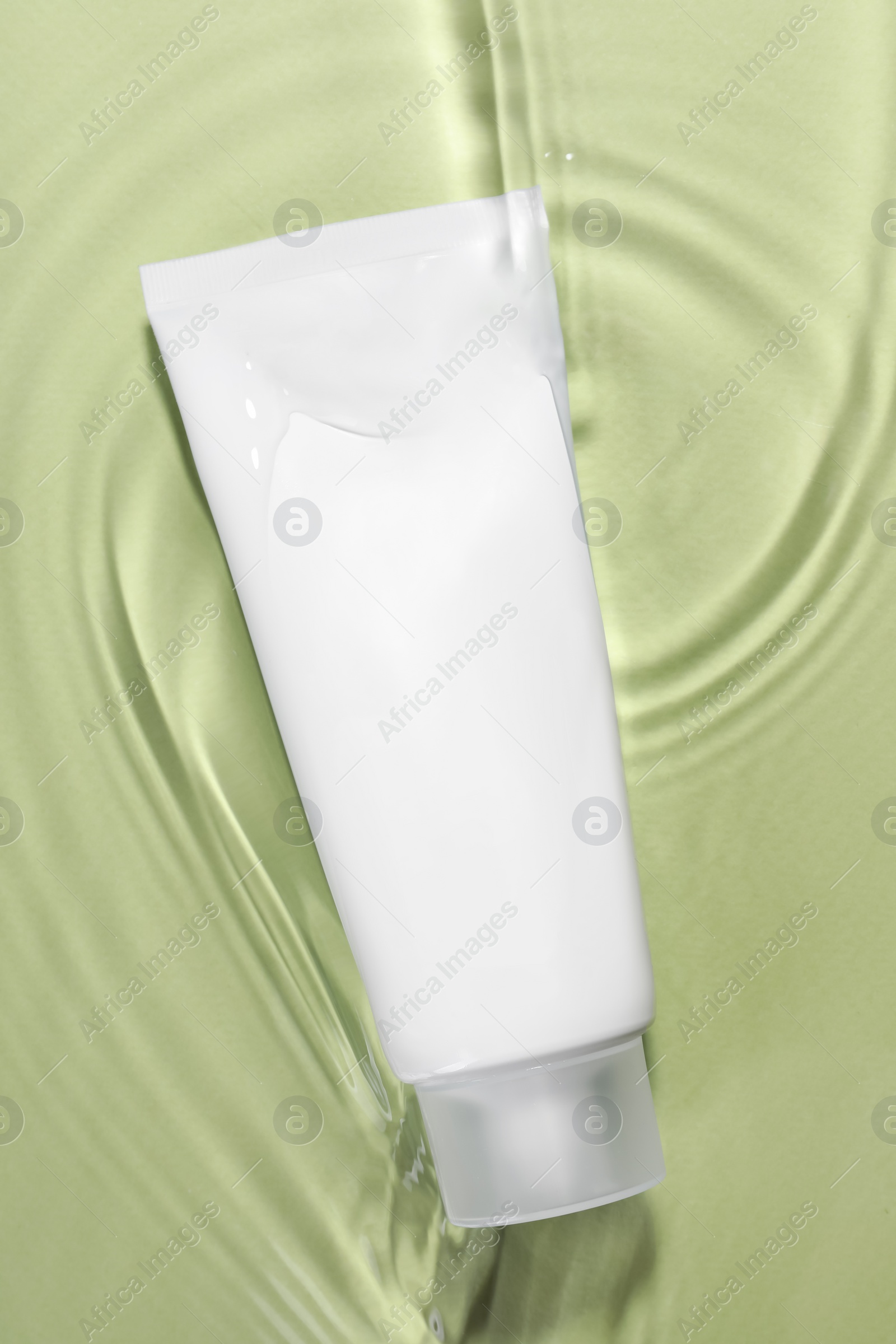 Photo of Tube of facial cleanser in water against olive background, top view