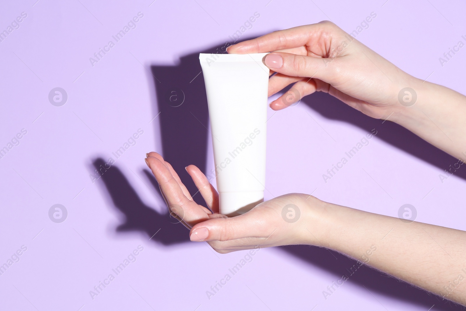 Photo of Woman holding tube of cream on violet background, closeup