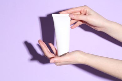 Woman holding tube of cream on violet background, closeup