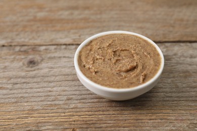 Photo of Delicious nut butter in bowl on wooden table, closeup. Space for text