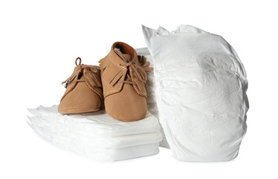 Photo of Disposable diapers and child's shoes on white background