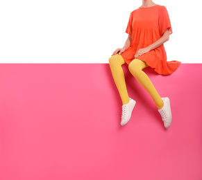 Woman wearing yellow tights and stylish shoes sitting on color background, closeup. Space for text