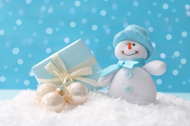 Cute toy snowman, gift box and Christmas balls on snow against blurred background