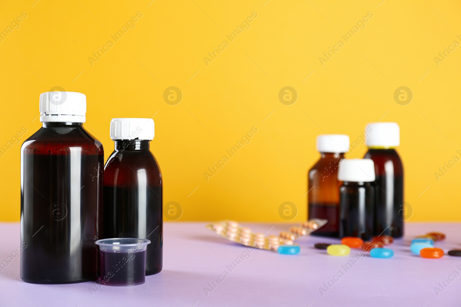 Photo of Bottles of cough syrup and measuring cup on color background. Space for text