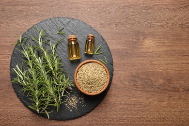Photo of Essential oil, fresh and dry rosemary on wooden table, top view. Space for text