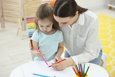 Photo of Mother and her little daughter drawing with colorful pencils at home