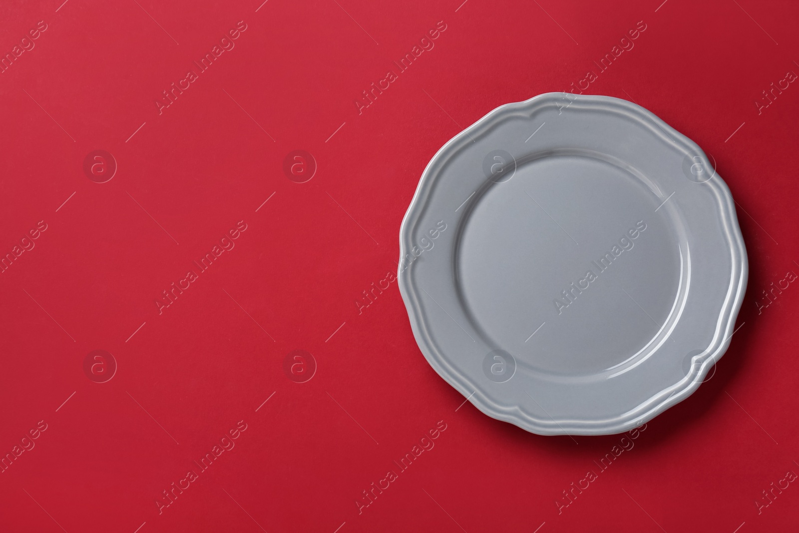 Photo of Clean grey plate on red background, top view. Space for text