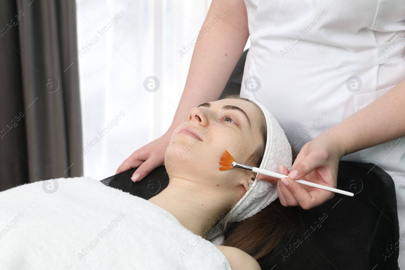 Photo of Cosmetologist with brush applying cosmetic product to client`s face in clinic, closeup