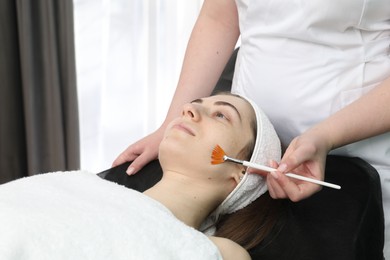 Cosmetologist with brush applying cosmetic product to client`s face in clinic, closeup