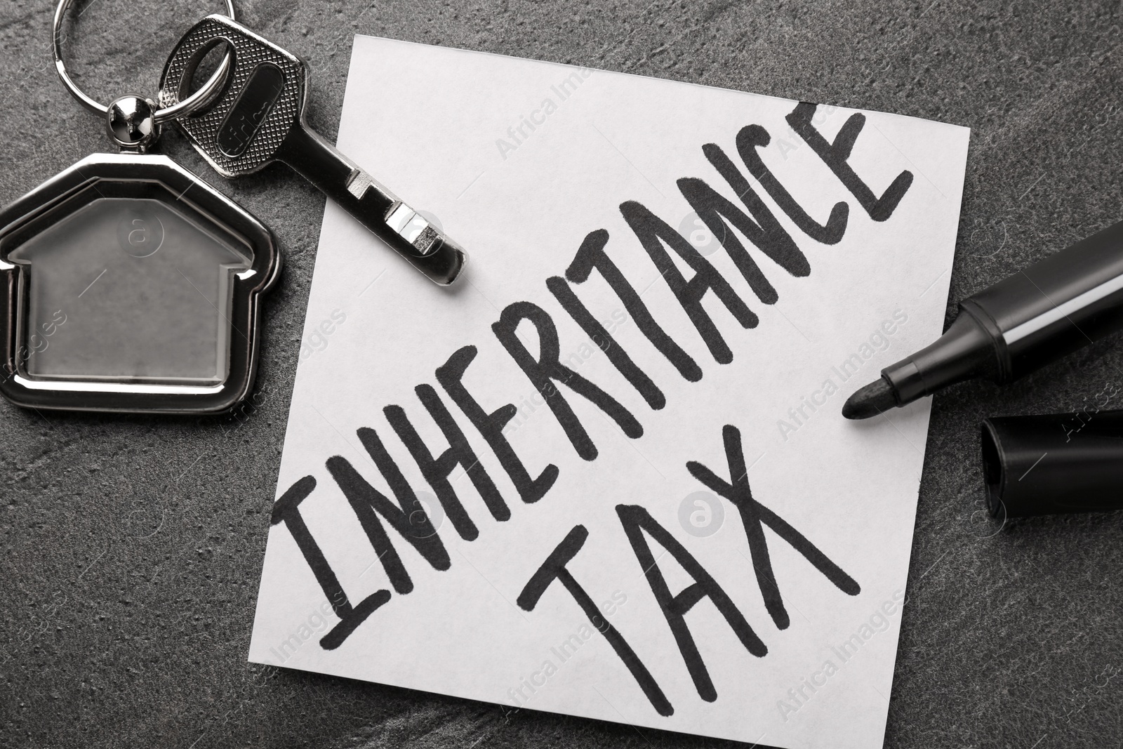 Photo of Inheritance Tax. Paper note, key with key chain in shape of house and marker on grey table, flat lay