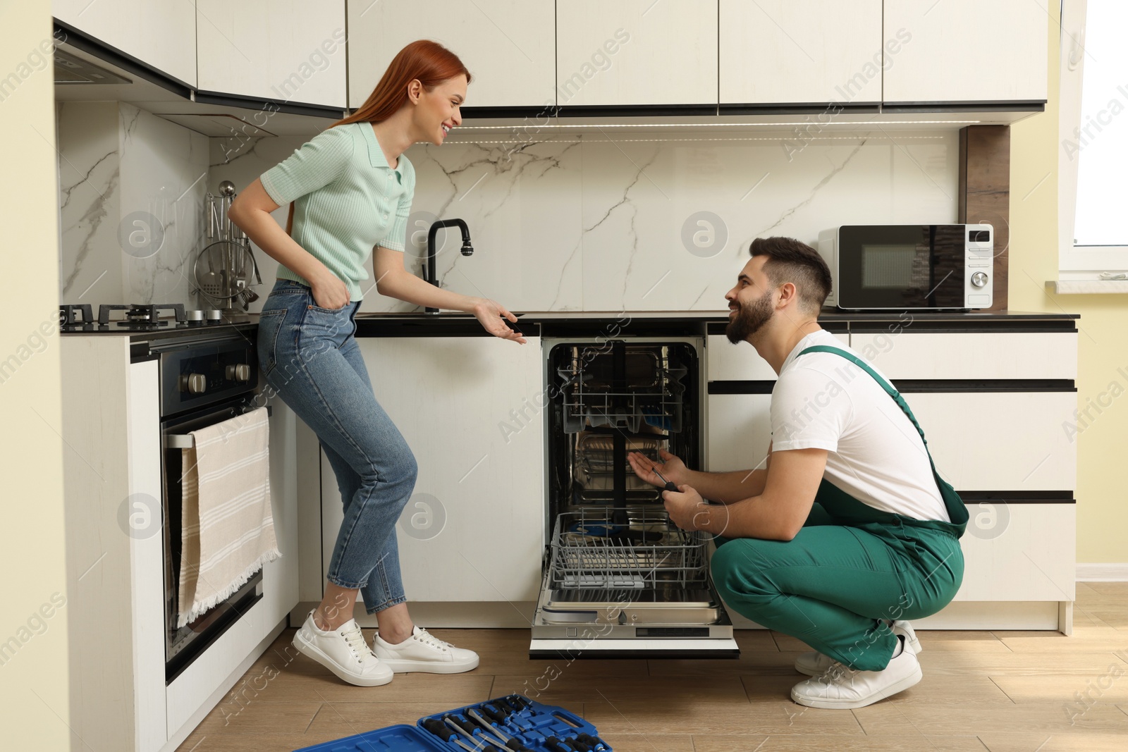 Photo of Smiling woman discussing with repairman near dishwasher in kitchen
