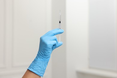 Doctor holding syringe with needle indoors, closeup view