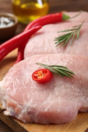 Photo of Pieces of raw pork meat, rosemary and chili peppers on board, closeup