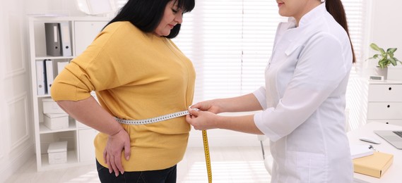 Image of Nutritionist measuring overweight woman's waist with tape in clinic. Banner design