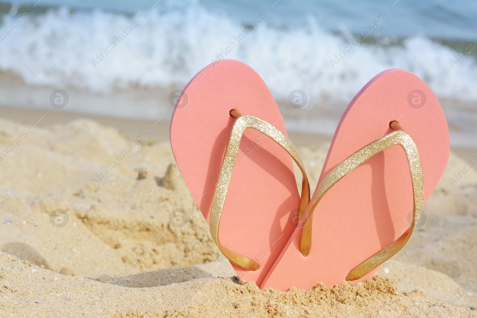 Photo of Stylish flip flops in sand on beach near sea, space for text
