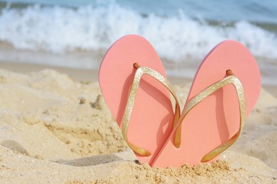 Photo of Stylish flip flops in sand on beach near sea, space for text