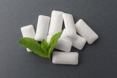Photo of Tasty white chewing gums and mint leaves on grey background, top view