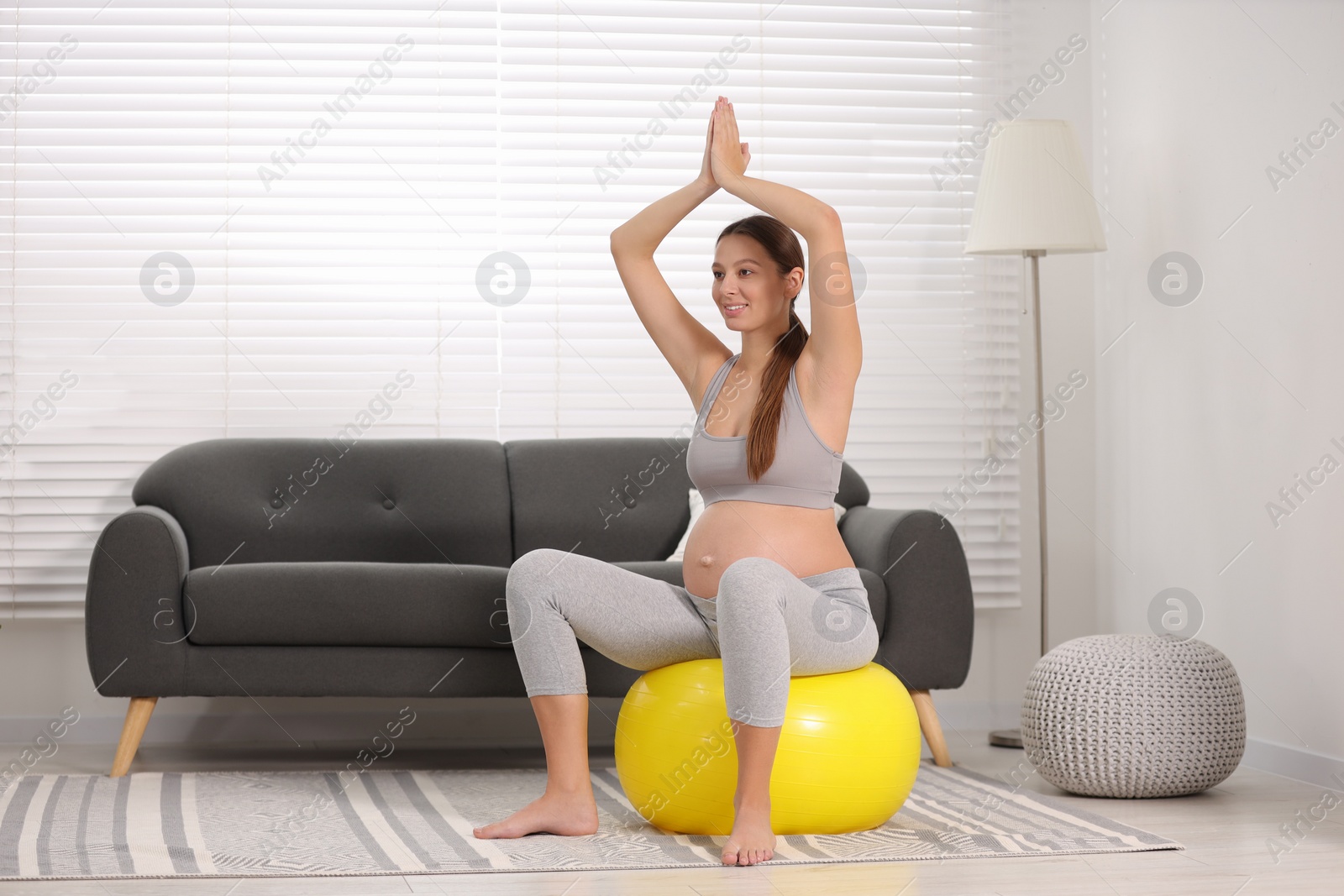 Photo of Pregnant woman doing exercises on fitness ball in room. Home yoga