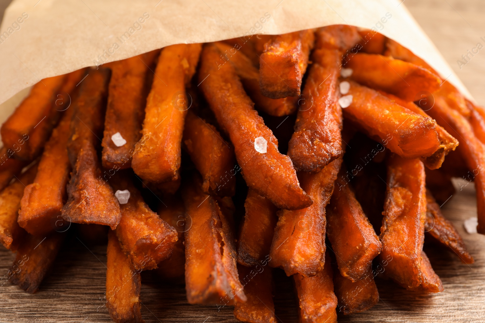 Photo of Paper bag with tasty sweet potato fries on table, closeup