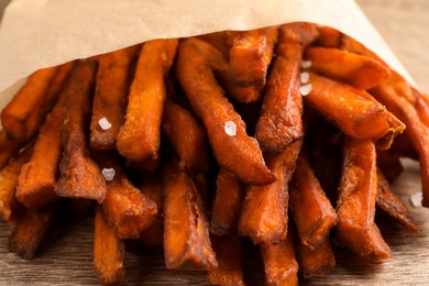 Photo of Paper bag with tasty sweet potato fries on table, closeup