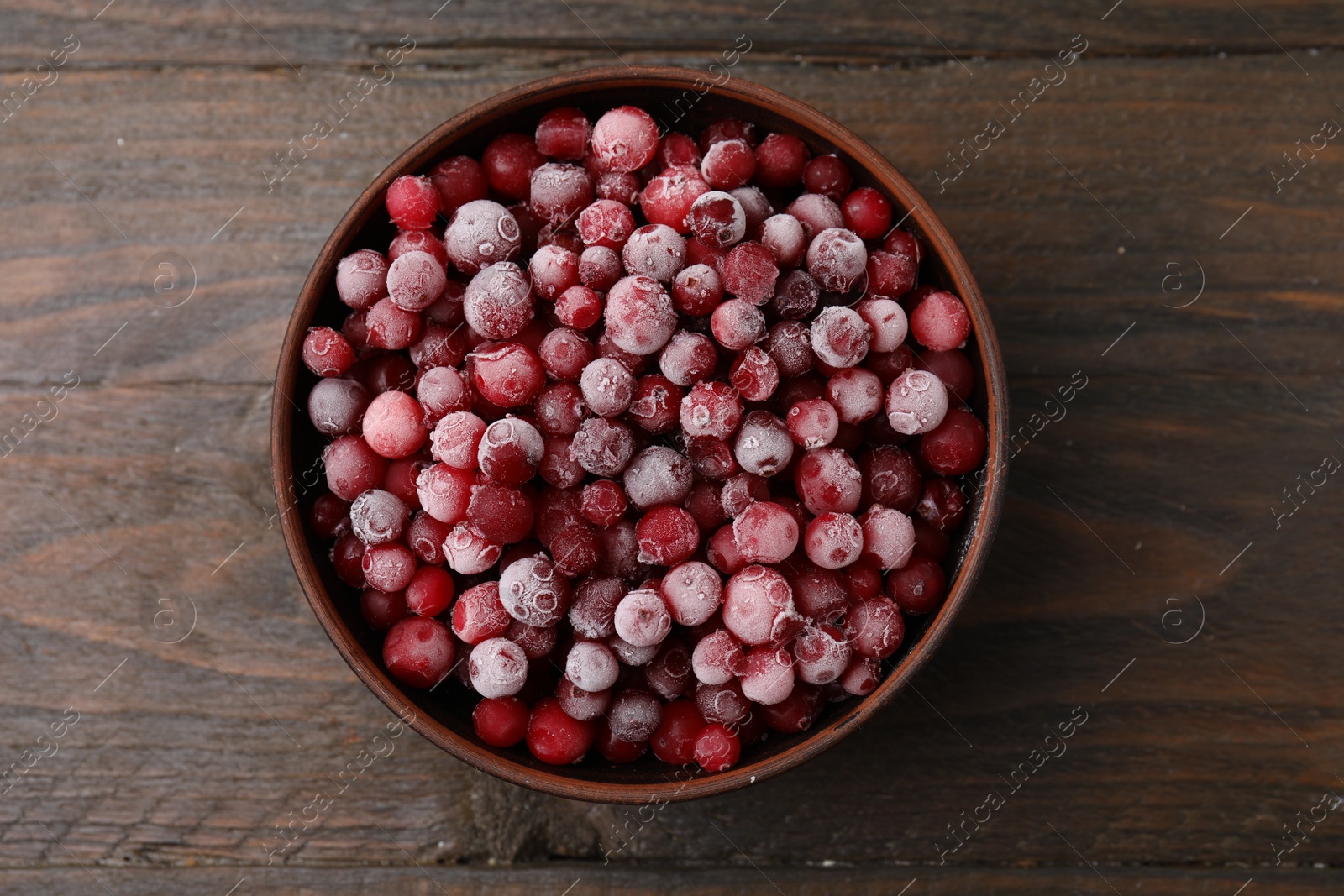 Photo of Frozen red cranberries in bowl on wooden table, top view