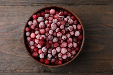 Photo of Frozen red cranberries in bowl on wooden table, top view