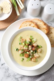 Photo of Tasty potato soup with croutons and green onion in bowl served on white marble table, flat lay