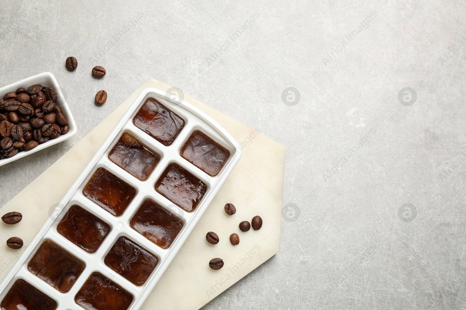 Photo of Ice cubes with coffee beans in tray on grey table, flat lay. Space for text